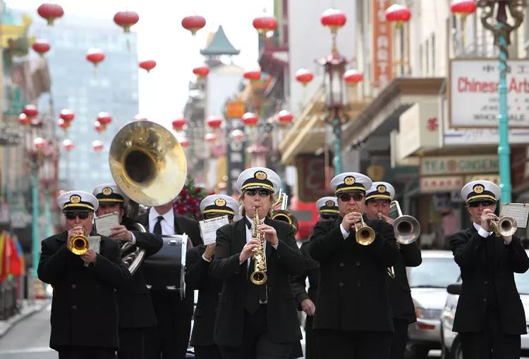 Green Street Memorial Band (formerly Green Street Mortuary Band) marching down a Chinatown street decorated with traditional red lanterns during a ceremonial procession honoring Vietnamese and Chinese funeral customs